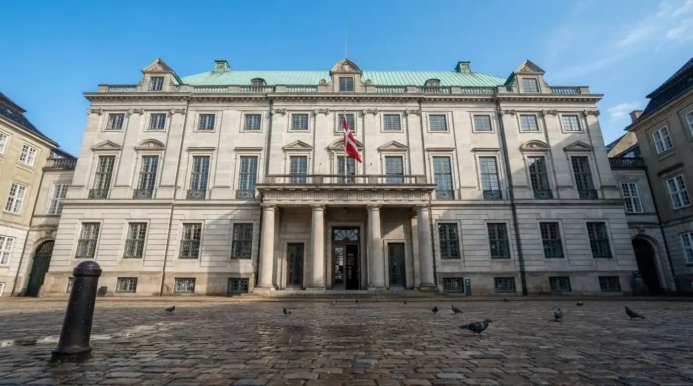 En historisk bygning i København med grøn kobbertag og kolonner i klart dagslys, set fra pladsen foran.